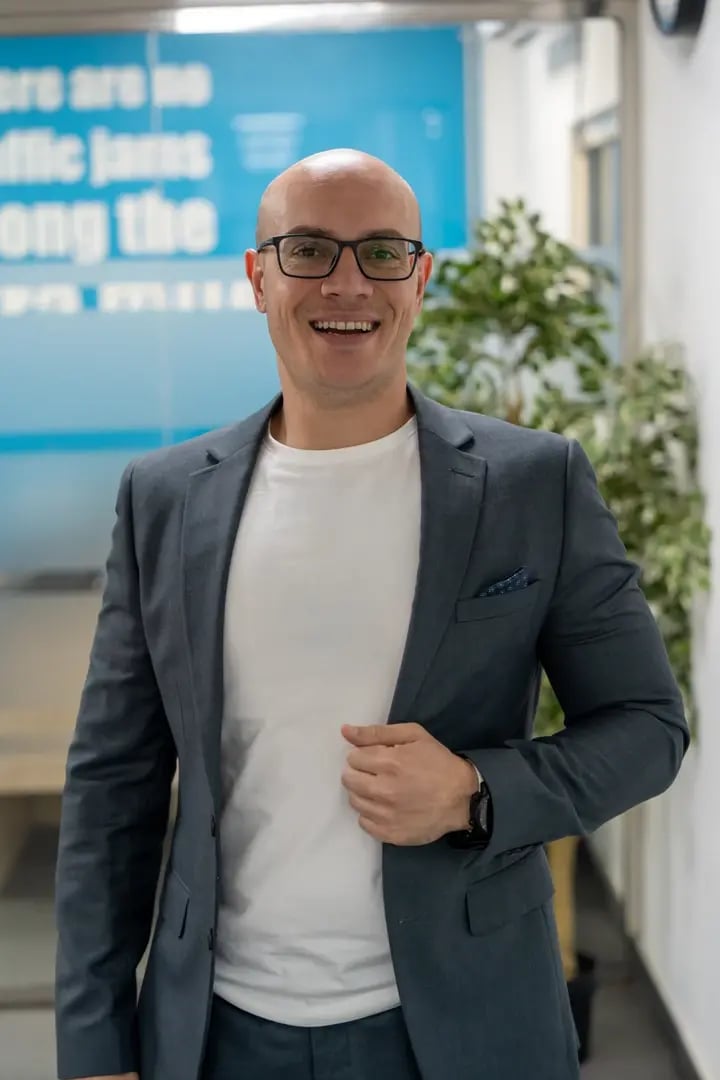 Professional man wearing glasses and gray blazer smiling in modern office with blue signage