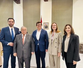 A formal group photo of five adults standing in a row indoors, dressed in professional business attire, including suits and blazers.