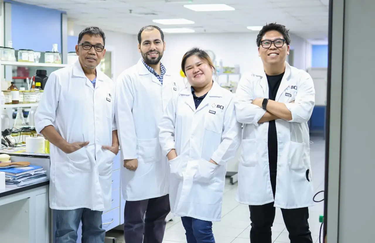 Four scientists in white lab coats posing together in modern research laboratory with equipment and shelving